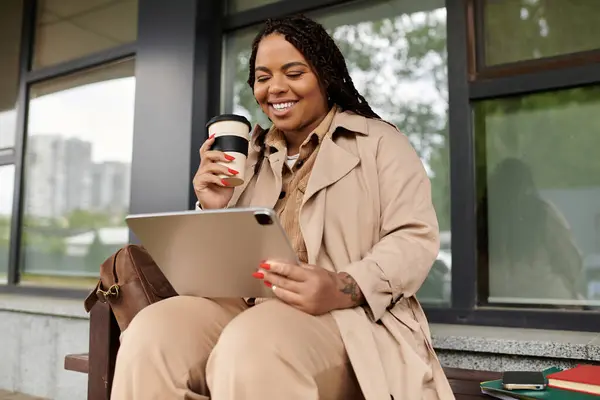 University teacher smiles while looking at a tablet and sipping coffee on campus bench. — Stock Photo