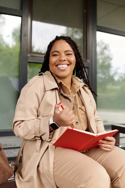 Une femme, professeur d'université, sourit vivement tout en tenant un cahier, profitant de la journée à l'extérieur. — Photo de stock