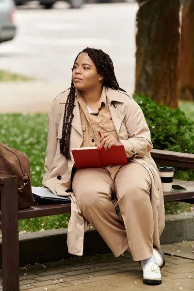 A university teacher reflects while seated on a bench in a peaceful park with her notebook. — Stock Photo