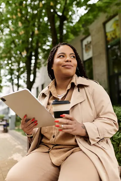 A university teacher relaxes outdoors in the city, sipping coffee and using a tablet. — Stock Photo