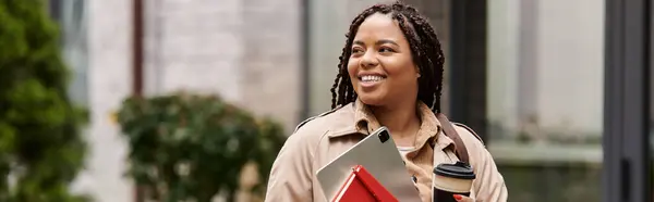 A woman in professional attire smiles while holding teaching materials and coffee at university. — Stock Photo