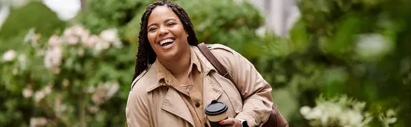 Woman walks joyfully with a coffee cup, surrounded by lush greenery on campus. — Stock Photo