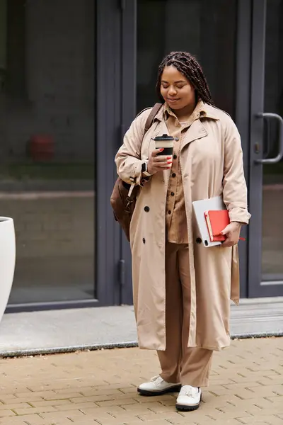 Mujer se para fuera de su edificio universitario, bebiendo café y revisando sus notas. - foto de stock