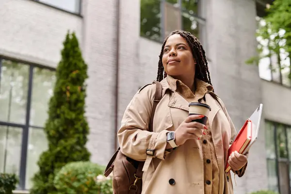 Woman enjoys a moment of reflection while carrying coffee and study materials on campus — Stock Photo