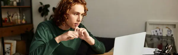 Junger Mann konzentriert sich auf seinen Laptop, während er gemütlich zu Hause sitzt und in seine Aufgaben vertieft ist. — Stockfoto