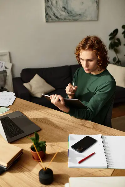 A young man is focused on his tablet, surrounded by a cozy home workspace and creative tools. — Stock Photo