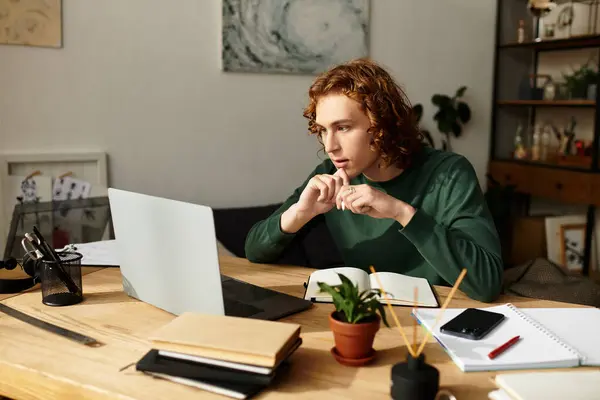 Un giovane uomo siede alla sua scrivania di legno, intensamente concentrato sul suo computer portatile, circondato da un arredamento accogliente. — Stock Photo