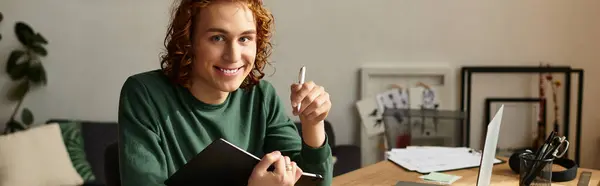 Smiling young man at home works on his notebook while comfortably seated at a desk. — Stock Photo
