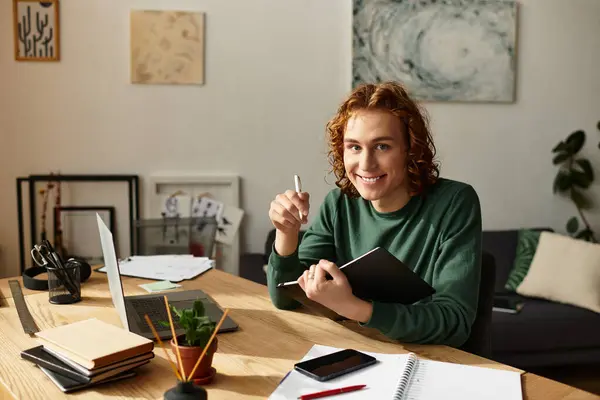 Um jovem senta-se em uma mesa de madeira, escrevendo em um caderno com um sorriso quente em um quarto acolhedor. — Fotografia de Stock