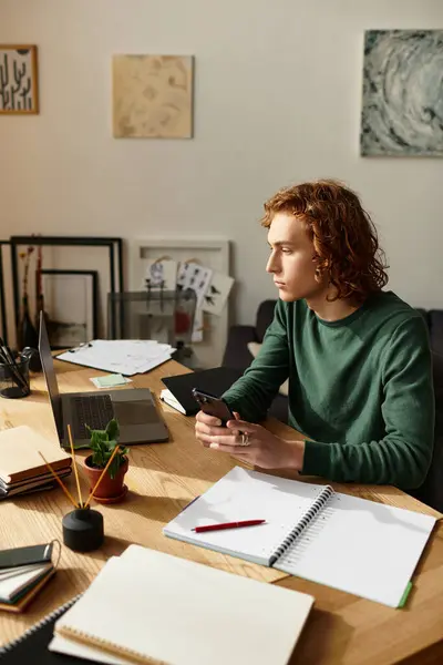 In uno spazio accogliente, un giovane uomo si concentra sul suo telefono, circondato da quaderni e forniture d'arte. — Foto stock