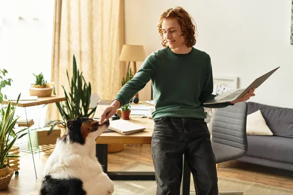 Young man enjoying a relaxing day at home, engaging affectionately with his pet dog and laptop. — Stock Photo