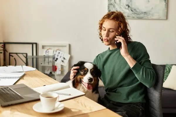 Um jovem conversa ao telefone em casa enquanto seu cachorro relaxa nas proximidades. — Fotografia de Stock