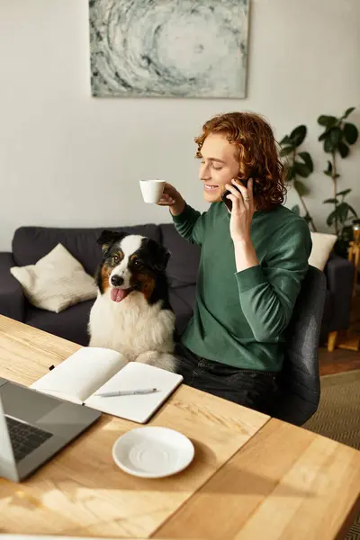 Joven hombre disfruta de un momento acogedor en casa mientras charla por teléfono con su perro a su lado. - foto de stock
