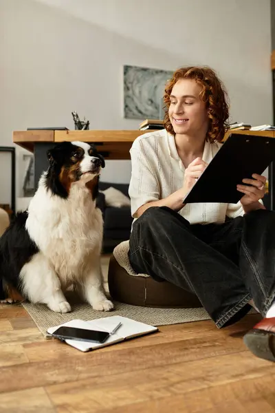 A young man smiles while sitting on a mat with his dog, capturing ideas in a cozy home environment. — Stock Photo