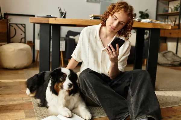 A young man relaxes on the floor, interacting with a smartphone while his dog lounges nearby. — Stock Photo