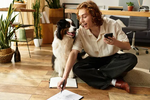 A young man sits comfortably on the floor with his dog, enjoying quality time while drawing. — Stock Photo