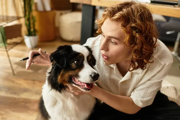 Um jovem se envolve brincando com seu cão em um ambiente acolhedor e confortável em casa enquanto segura uma caneta. — Fotografia de Stock