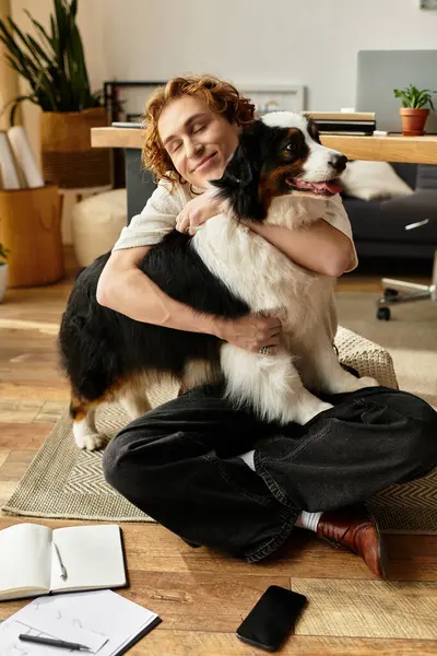 A young man sits comfortably on the floor, embracing his joyful dog while sharing a warm connection. — Stock Photo