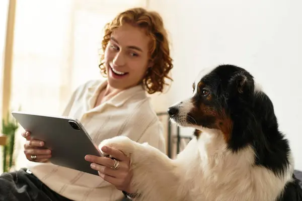 Relaxing at home, a young man shares a joyful moment with his dog while using a tablet. — Stock Photo