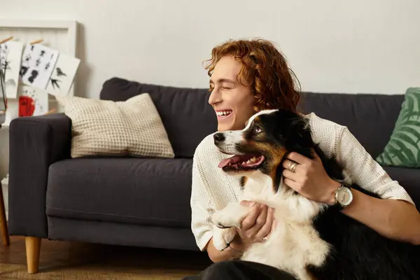 Jovem sorridente brinca com seu cão carinhoso em uma acolhedora sala de estar cheia de calor. — Fotografia de Stock