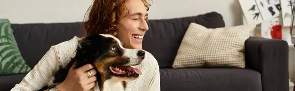 A young man smiles brightly while cuddling his loving dog in a comfortable living space. — Stock Photo