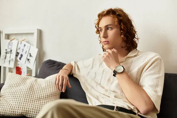 A young man sits on a sofa in his comfortable home, lost in thought and deep contemplation. — Stock Photo