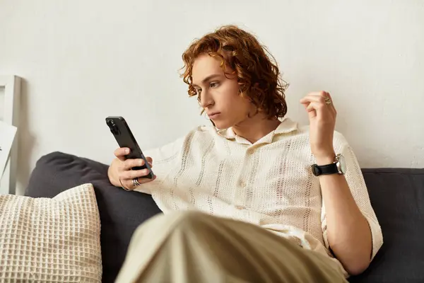 Un joven se relaja en un sofá en casa, absorto en su smartphone. - foto de stock