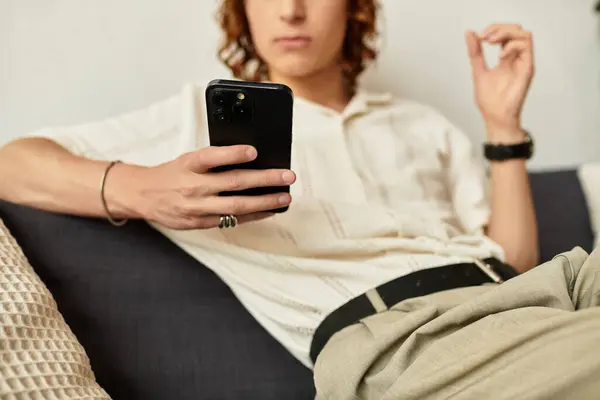 A young man sits comfortably at home, engaged with his smartphone in a warm atmosphere. — Stock Photo