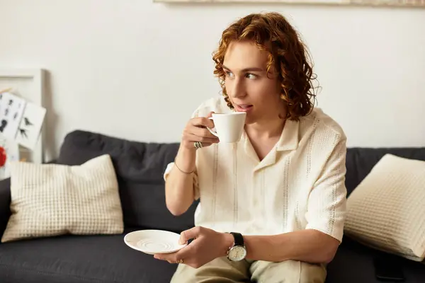 Ein junger Mann nippt nachdenklich an seinem Drink, umgeben von einer gemütlichen Atmosphäre in seinem Haus. — Stockfoto