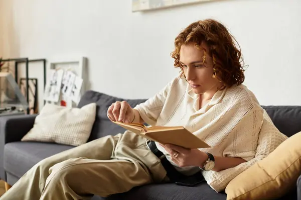 A young man relaxes at home, diving into the pages of an intriguing book while lounging comfortably. — Stock Photo