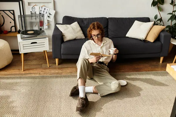 A young man relaxes at home, sipping coffee and reading his book while sitting comfortably. — Stock Photo