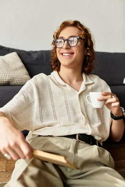Un giovane uomo si gode il suo tempo a casa, sorseggiando una bevanda calda con un sorriso allegro. — Foto stock