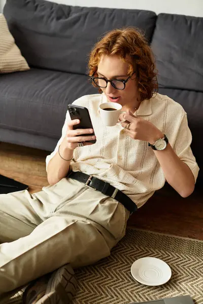 Acogedores momentos se desarrollan como un joven sorbe café, comprometido con su teléfono en casa, sintiéndose relajado. - foto de stock