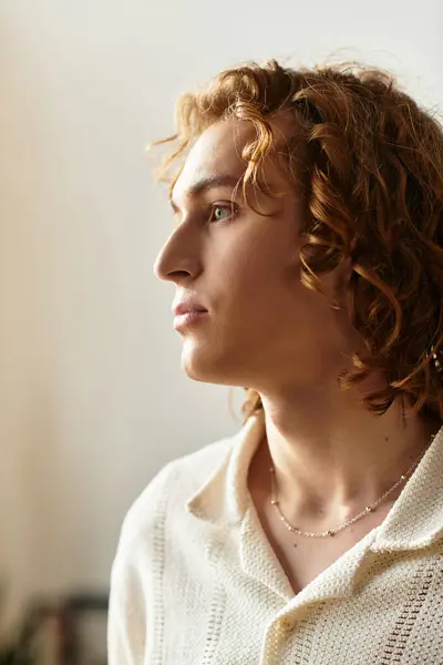 Ein junger Mann mit lockigem Haar sitzt zu Hause, verloren in Gedanken, während er eine gemütliche Atmosphäre genießt. — Stockfoto