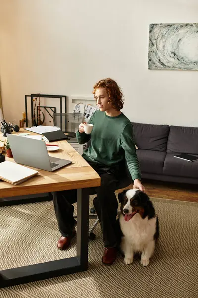 Young man enjoys a warm drink while working at his stylish desk, connecting with his dog. — Stock Photo