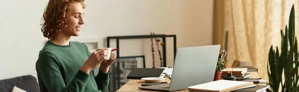 Un joven bebe café en su acogedor escritorio, enfocado en su portátil en un espacio cálido. - foto de stock