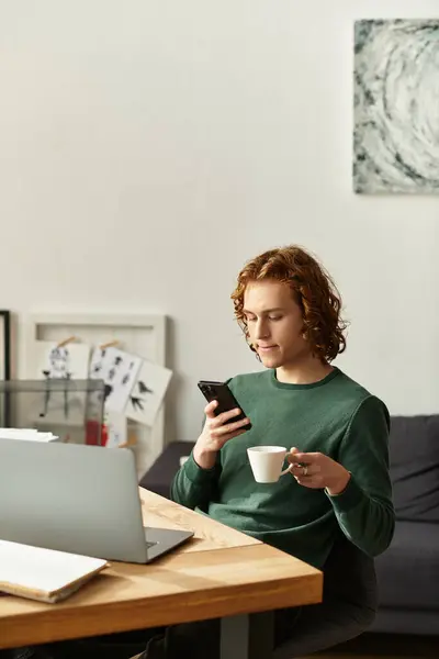 Giovane rilassato si siede a casa, sorseggiando caffè e impegnandosi con il suo smartphone durante il giorno. — Foto stock