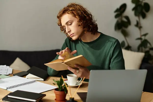 Focused young man reads intently while seated at a warm, inviting table in his home. — Stock Photo