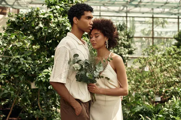In a lush greenhouse, a young couple shares a tender moment amidst the greenery, filled with love. — Stock Photo