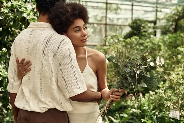 A loving couple shares a tender moment in a greenhouse filled with thriving plants and greenery. — Stock Photo