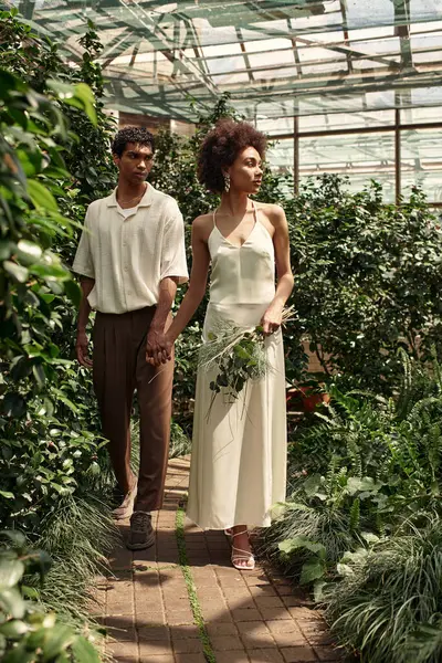 In a vibrant greenhouse, a young couple strolls, enjoying joyful moments among the plants. — Stock Photo