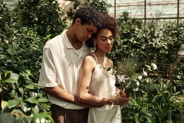 A loving couple stands close together amidst a thriving greenhouse, surrounded by lush plants. — Stock Photo
