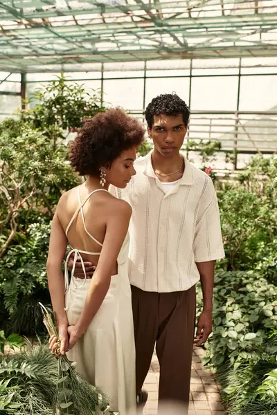 Loving couple poses affectionately amidst lush plants in a peaceful greenhouse setting. — Stock Photo