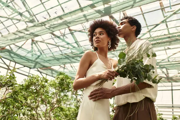 In a beautiful greenhouse, a young couple enjoys a loving embrace amid vibrant plants and greenery. — Stock Photo