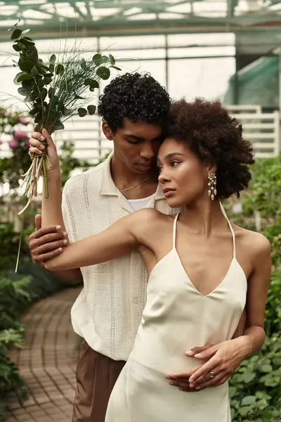 In a serene greenhouse, a young couple embraces tenderly among thriving plants, radiating love. — Stock Photo