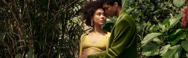 Una joven pareja se abraza tiernamente, rodeada de una próspera variedad de plantas y vegetación. - foto de stock
