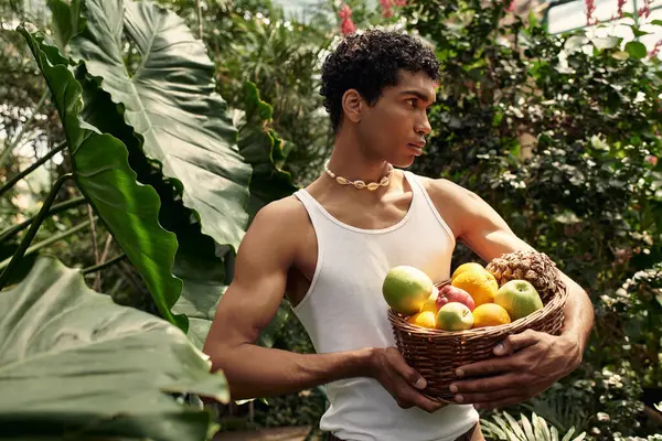 Young stylish man enjoys a good moment amid rich greenery, surrounded by colorful fruits and plants. — Stock Photo