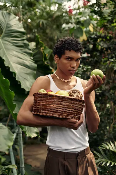 Young stylish man explores a vibrant greenhouse, expressing himself and collecting fresh fruits. — Stock Photo