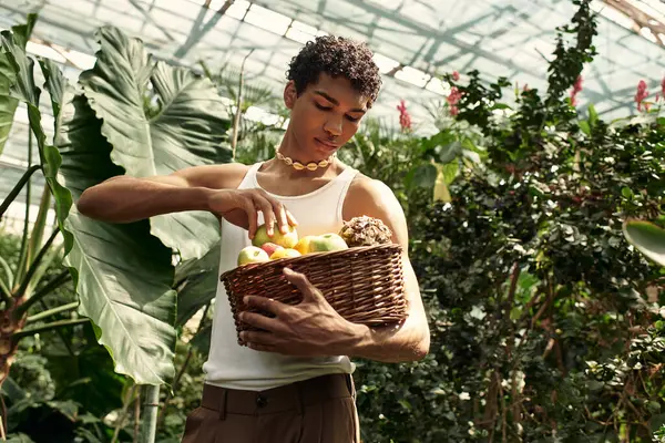 A young stylish man posing actively in a greenhouse, surrounded by greenery and fresh produce. — Stock Photo