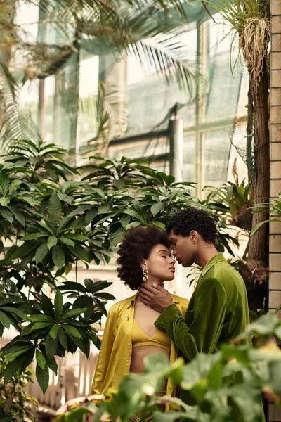 In a vibrant greenhouse, a young couple embraces intimately amid lush plants, radiating love. — Stock Photo